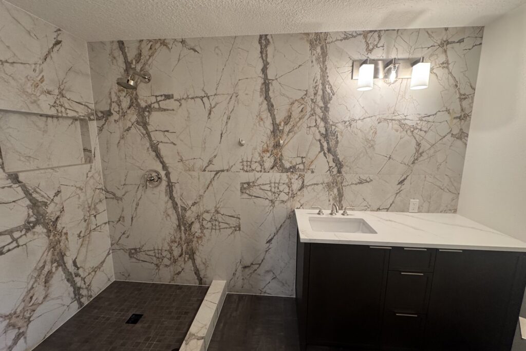 Bathroom remodel with large marble-look tile, open shower and vanity lighting
